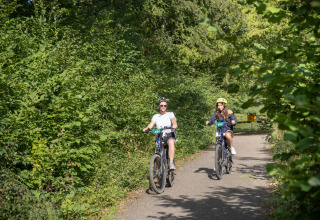 Twee personen fietsen op een bosrijk pad in Huttopia Vallée de la Semois vakantiepark, Namen, België.