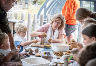 Børn og voksne former ler sammen ved et kreativt værksted i Huttopia Vallée de la Semois, Belgien.