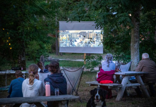 Noche de cine al aire libre en Huttopia Vallée de la Semois, Namur, Bélgica, con gente viendo una película.