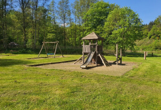 Legeplads med rutsjebane og gynger i en grøn park omgivet af træer på Huttopia Vallée de la Semois, Belgien.