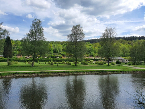 Photo of a river with green trees and holiday cabins in the background at Huttopia Vallée de la Semois, Belgium.