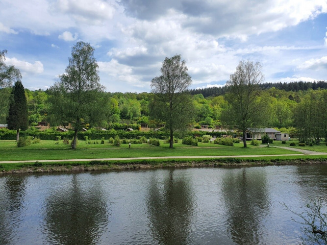Photo of a river with green trees and holiday cabins in the background at Huttopia Vallée de la Semois, Belgium.