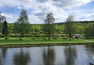 Foto di un fiume con alberi verdi e bungalow sullo sfondo a Huttopia Vallée de la Semois, Namur, Belgio.