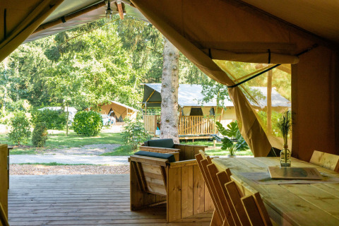 Blick aus einem Safarizelt auf Camping La Colline in Belgien mit Holzmöbeln und grünem Außenbereich.