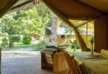 View from inside a safari tent at Camping La Colline in Belgium, with wooden furniture and lush greenery outside.