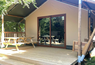 Houten hut met overdekt terras en picknicktafel in Urban-Gardens Ieper vakantiepark, West-Vlaanderen, België.