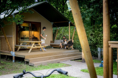 Familia relajándose en el porche de una tienda glamping en Urban-Gardens Ieper, parque en Flandes Occidental, Bélgica.