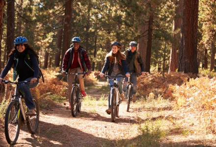 Four friends biking on a forest trail at a holiday park, enjoying the outdoors near glamping tents.