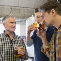 Tres hombres degustan y huelen cerveza en una cervecería, observando atentamente las bebidas en sus vasos.