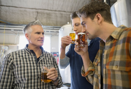 Tres hombres degustan y huelen cerveza en una cervecería, observando atentamente las bebidas en sus vasos.
