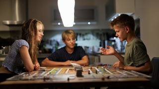 Tres jóvenes juegan a un juego de mesa en una cocina acogedora de un parque vacacional tipo glamping.