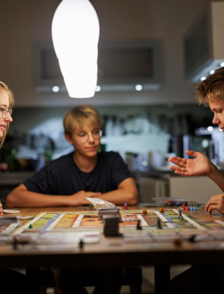 Tres jóvenes juegan a un juego de mesa en una cocina acogedora de un parque vacacional tipo glamping.