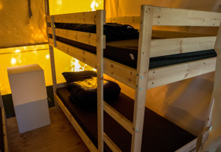 Interior de una tienda safari con literas de madera en Camping het Swinnenbos en Bélgica, iluminación cálida.