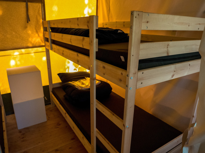 Interior de una tienda safari con literas de madera en Camping het Swinnenbos en Bélgica, iluminación cálida.