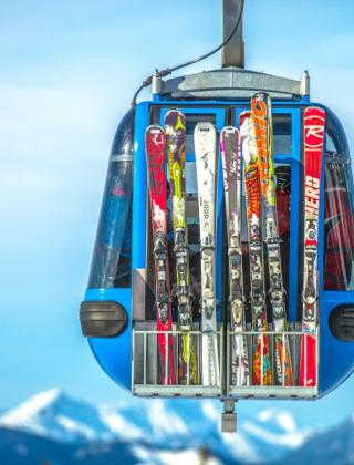 Telecabina suspendida con esquís sujetos afuera, sobre montañas nevadas y cielo azul en invierno.