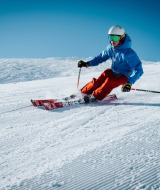 Un esquiador baja rápidamente por una pendiente nevada bajo un cielo azul claro y lleva ropa colorida.