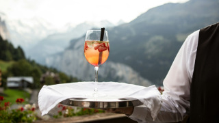 Een ober serveert een fruitige cocktail in een glamping park, met bergen en natuur op de achtergrond.