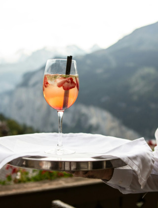 Un camarero sirve un cóctel refrescante con fresas, naturaleza y montañas al fondo en un parque glamping.