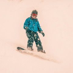 A person snowboarding down a snowy slope at a holiday park offering glamping accommodations.