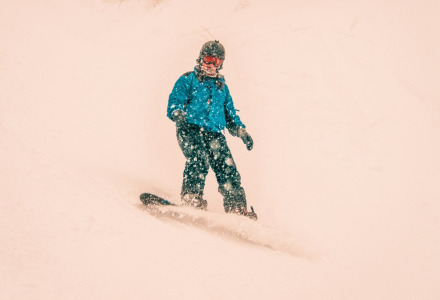 Persona practicando snowboard en una pendiente nevada en un parque vacacional con glamping.