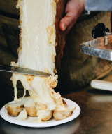 Du fromage fondu est raclé d'une meule sur des pommes de terre dans un parc de vacances glamping.