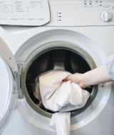 Una persona mete sábanas blancas en una lavadora en Les Chalets Huttopia de Font-Romeu, Occitania, Francia.