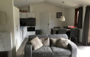 Living area with grey sofa, kitchen, and dining table in Boekhorst 4 lodge at De Achterhoek, Netherlands.