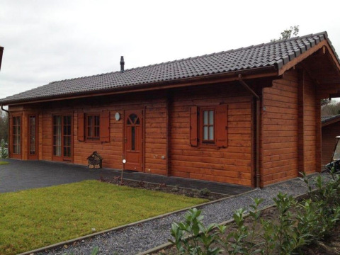 Een foto van een sfeervolle houten lodge met donker pannendak, gazon en grindpad, overdag genomen.