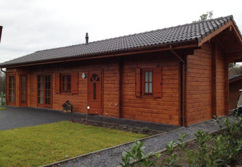 Photo d’un chalet en bois chaleureux avec toit sombre, pelouse verte et sentiers en gravier au premier plan.