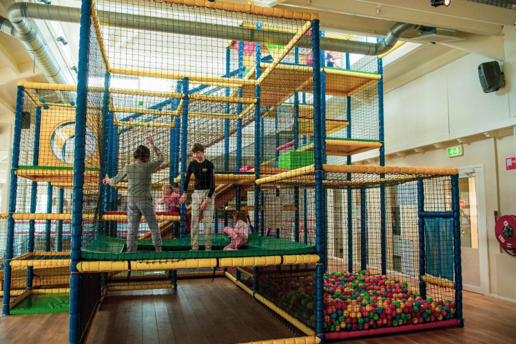 Niños jugando en un parque infantil cubierto con estructuras y piscina de bolas en un alojamiento glamping.