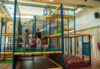 Niños jugando en un parque infantil cubierto con estructuras y piscina de bolas en un alojamiento glamping.