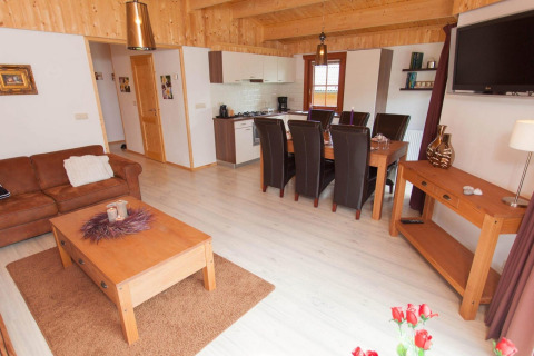 Gezellige lodge woonkamer met open keuken, eettafel, leren bank, houten meubels en lichte vloer.