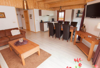 Gezellige lodge woonkamer met open keuken, eettafel, leren bank, houten meubels en lichte vloer.