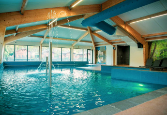 Indendørs swimmingpool med springvand og liggestole i et glampingresort omgivet af store vinduer.