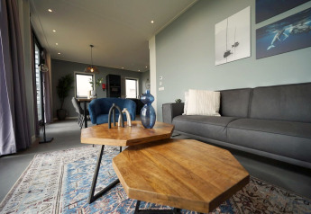 Moderne stue i Mode 6-lodgen, De Achterhoek, Holland med stilfuldt interiør, grå sofa og træborde.