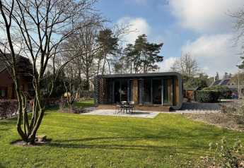 Modus Sauna 4 lodge met modern design en grote ramen, gelegen in een groene tuin tussen de bomen.