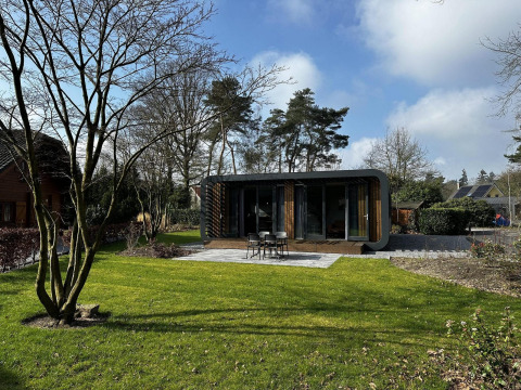 Moderne Modus Sauna 4 lodge met grote ramen in een groene tuin, omringd door bomen en open hemel.