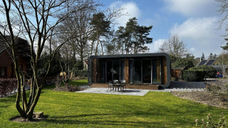 Lodge Modus Sauna 4 moderne avec grandes fenêtres, située dans un jardin vert entouré d’arbres et ciel.