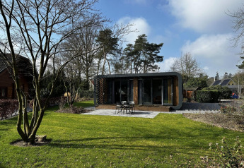 Moderne Modus Sauna 4 lodge met grote ramen in een groene tuin, omringd door bomen en open hemel.