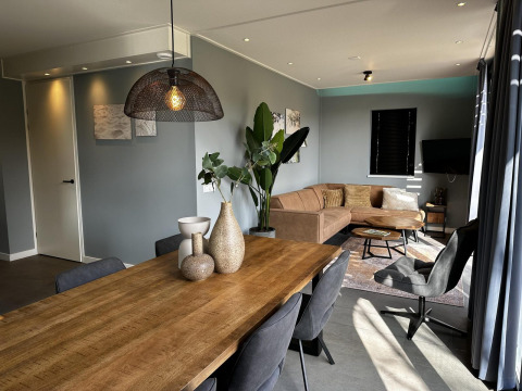 Moderne lodge stue i Modus Sauna 4, De Achterhoek, Nederlandene, med træbord, sofa og lysindfald.