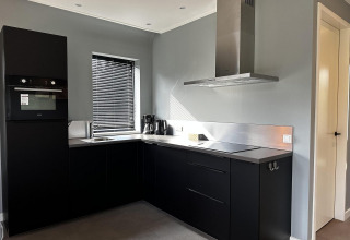 Cucina nera moderna a Modus Sauna 4, De Achterhoek, Paesi Bassi, con forno, cappa e veneziana alla finestra.