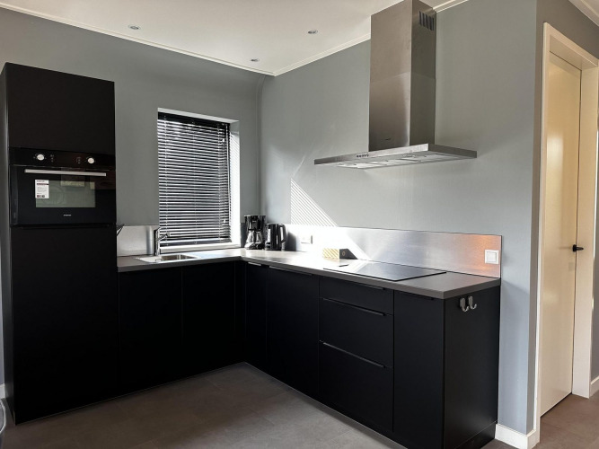Modern black kitchen at Modus Sauna 4, De Achterhoek, Netherlands, featuring oven, hood, and window blinds.