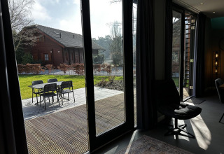Blick aus einer modernen Lodge mit großen Fenstern auf Terrasse und Garten in Modus Sauna 4, De Achterhoek, Niederlande.