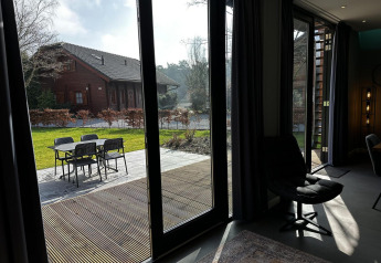 Gezicht vanuit een moderne lodge met grote ramen op terras en tuin bij Modus Sauna 4, De Achterhoek, Nederland.