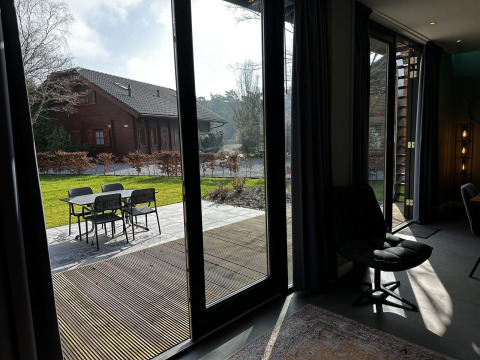 Blick aus einer modernen Lodge mit großen Fenstern auf Terrasse und Garten in Modus Sauna 4, De Achterhoek, Niederlande.