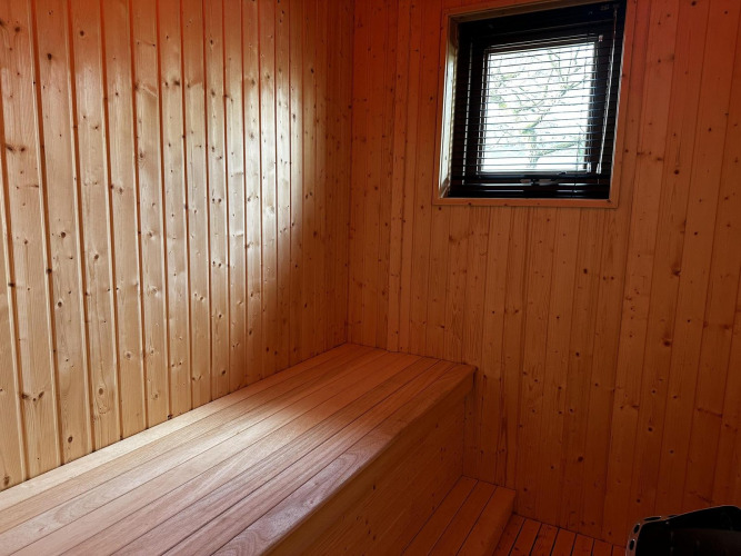 Wood-paneled interior of Modus Sauna 4 at De Achterhoek in the Netherlands, featuring a bench and window.