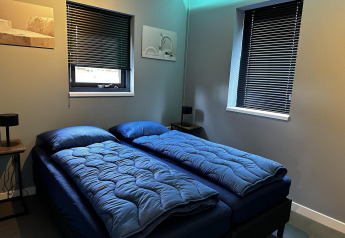 Dormitorio moderno con dos camas individuales, ropa de cama azul, persianas oscuras y decoración minimalista.