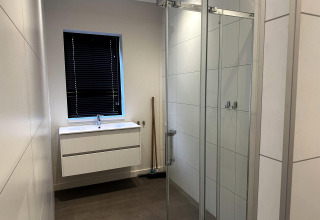 Moderne badkamer met witte wastafel, donkere jaloezieën en glazen douche in Modus Sauna 4, De Achterhoek, Nederland.