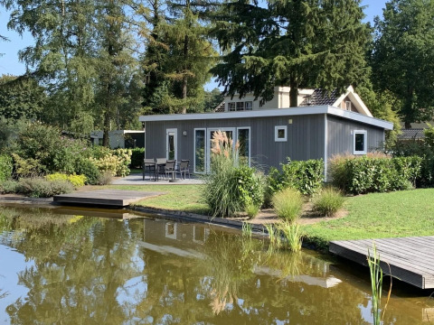 Pavilion 4 Lodge mit modernem grauem Design, umgeben von Grün und einem Teich im Vordergrund.
