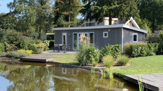 Pavilion 4 lodge met een modern grijs ontwerp, omgeven door veel groen en een vijver op de voorgrond.